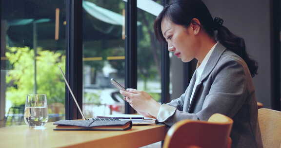 女商人坐在咖啡馆窗户边办公用电脑手机