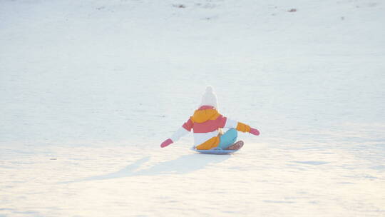 孩子坐在雪盘上从雪山上滑下来