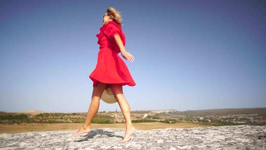 红裙草帽女子站在岩石上享受新鲜空气拥抱自