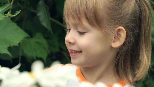 带花的小有趣女孩闻到洋甘菊的味道，看着相