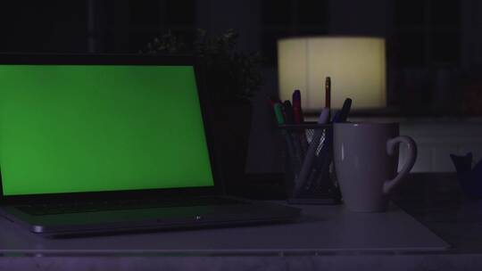 带绿屏的笔记本电脑。黑暗的办公室。多莉拍摄。非常适合放你自己的图像或视频。