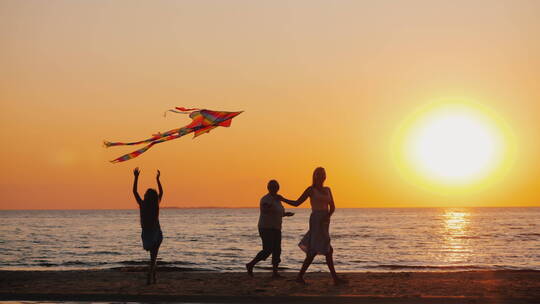 黄昏下在海边放风筝的一家人
