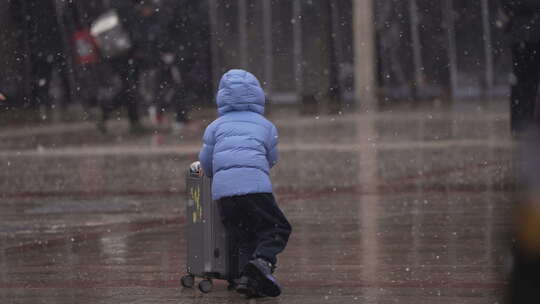大雪中兴奋地推行李箱的小孩