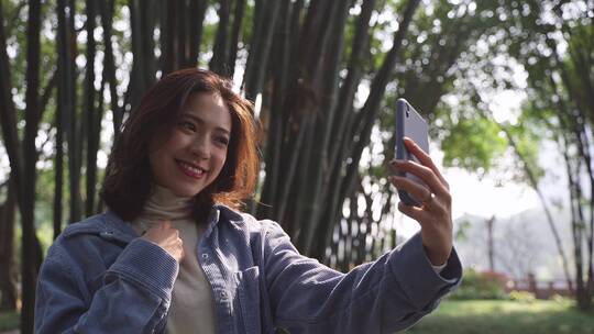 美女拿着手机在春天公园里自拍视频素材模板下载
