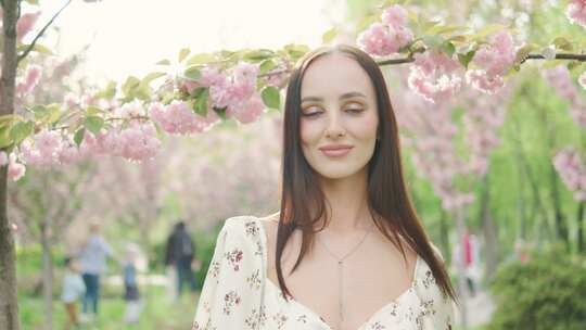 美丽的年轻女子在盛开的樱花树旁摆姿势，脸