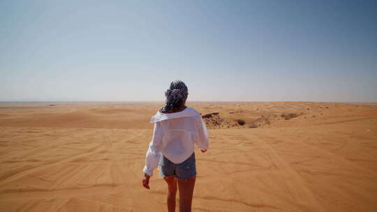 戴着围巾和太阳镜在沙漠沙丘上散步的年轻高加索女人