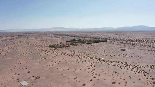 在加利福尼亚贫瘠的莫哈韦沙漠中，零散的沙漠房屋的上升和平移航拍。