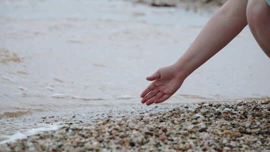 女人用手穿过肮脏的海水和岸上的鹅卵石特写