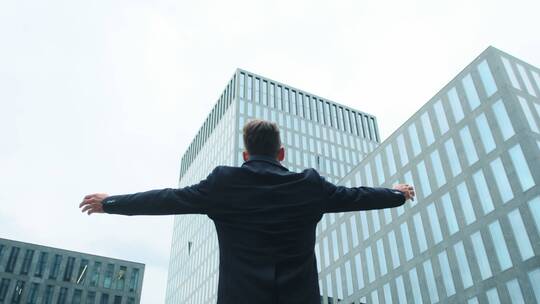 男人举起双臂站在玻璃摩天大楼前