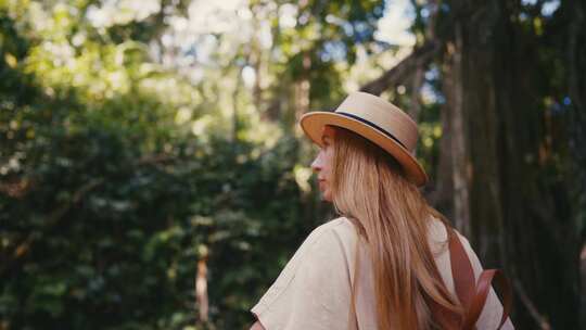 在绿色公园散步的旅游妇女戴着草帽背着背包