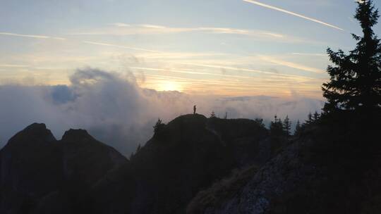 日落时分站在云层上的悬崖上的人