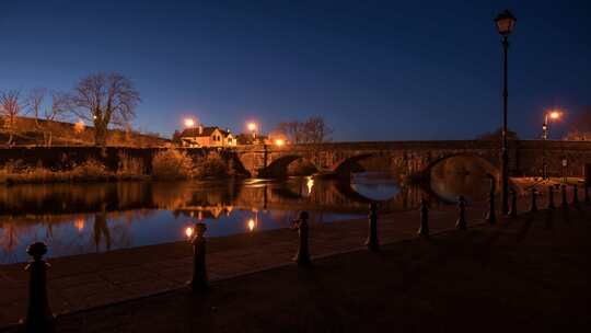 圣杯或白天到晚上的时间流逝的城镇村庄，沿河有桥和路灯