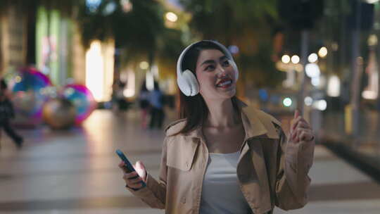 快乐可爱的亚洲女孩戴着耳机走在外面的晚上