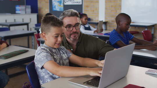 多样化的男老师帮助一个坐在教室里的男生使用笔记本电脑