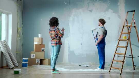 非裔美国妇女正在给男房子画家指路用白色油漆粉刷墙壁