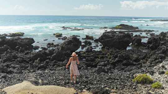 穿着碎花连衣裙在海边附近的黑色岩石上行走视频素材模板下载