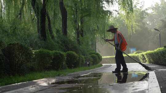 公园里清晨阳光中清扫道路积水的清洁工人