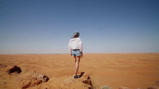 站在岩石山顶俯瞰广阔沙漠的年轻女子