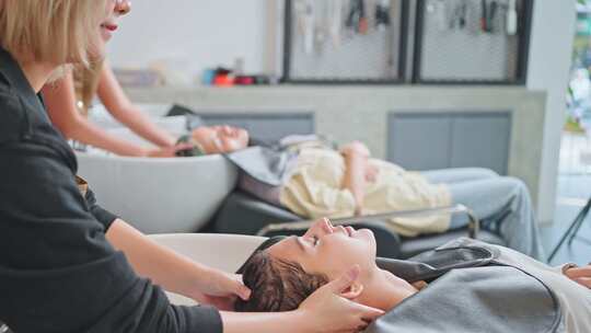 亚洲年轻女子躺在沙龙洗床上，在美容师的美发沙龙洗头。