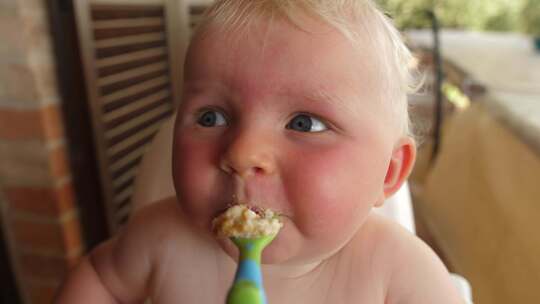 婴儿在户外高脚椅上用手持勺子吃饭
