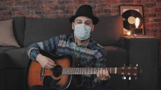 戴着医用面罩在家弹吉他的男人