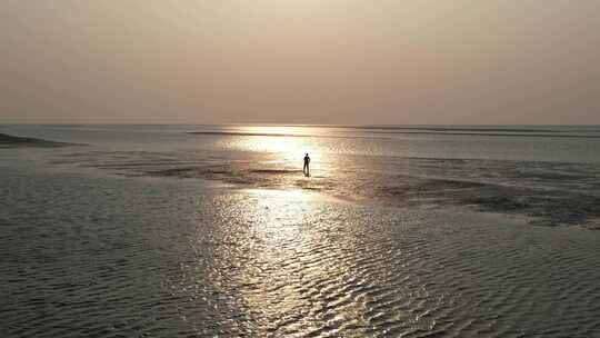 一个人行走在夕阳照耀下的沙滩上