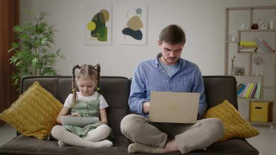 数字一代父亲在笔记本电脑上工作，女儿在平