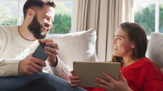 幸福的高加索夫妇坐在沙发上使用平板电脑和智能手机的视频视频素材模板下载