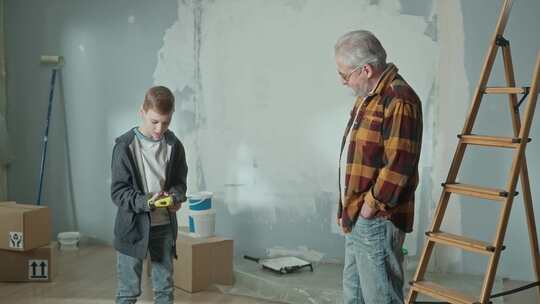 爷爷正在给他孙子看电动无绳螺丝刀是如何工作的