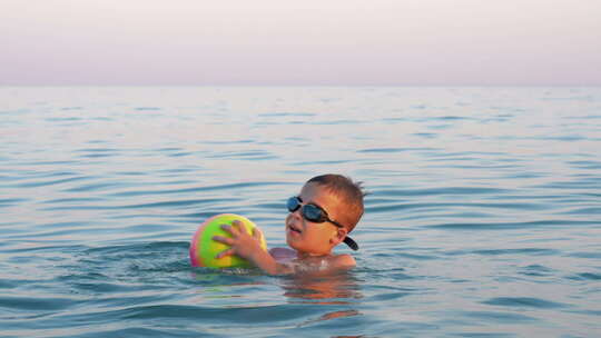 快乐的孩子带着球在海里游泳