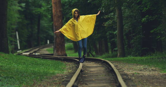 女人穿着雨衣走在旧铁路上