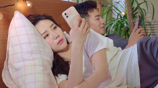 青年情侣坐在床上各自玩手机