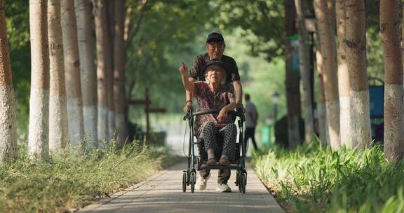 老年丈夫推着坐在轮椅上的妻子在公园散步