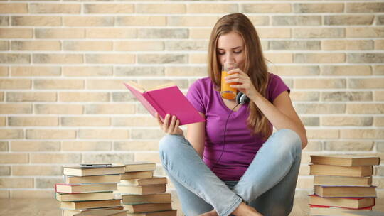 女孩坐在地板上看书喝果汁