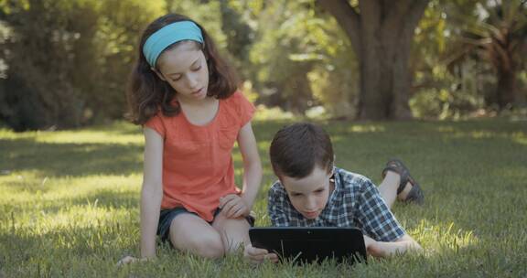 女孩和弟弟在草地上玩电脑