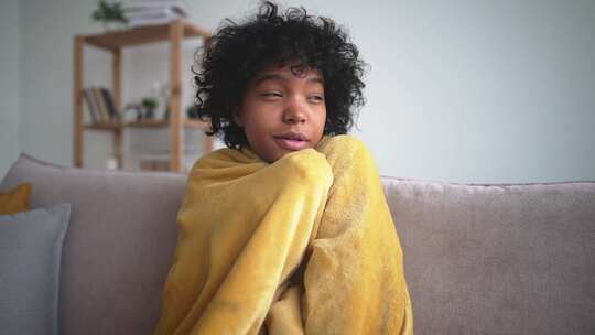 生病美丽的非裔美国年轻女子坐在家里的沙发上发烧