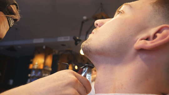 理发店专业理发师用电动剃须刀修剪年轻顾客胡须的男性手视频素材模板下载