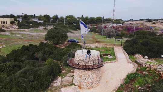 空中旋转拍摄的以色列国旗飘扬在以色列的一座石头纪念碑上，白天的Katzir