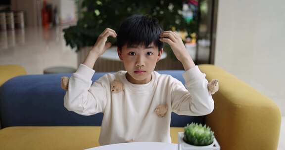 可爱的中国小男孩坐在沙发上抓头发