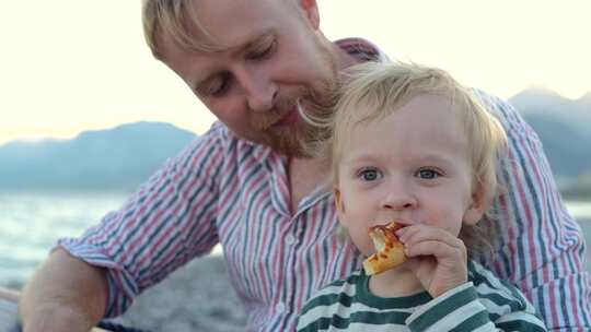肖像儿子和父亲在海滩上吃披萨