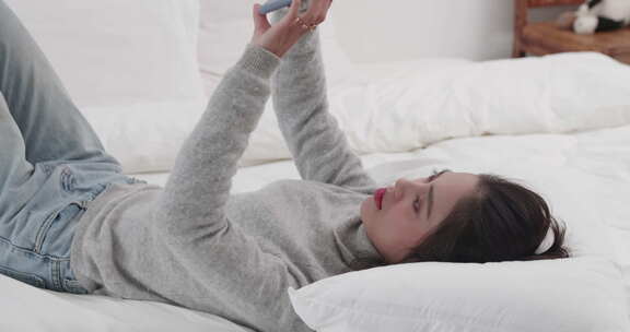 年轻美女开心躺在床上玩手机