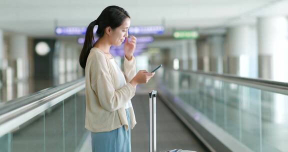 妇女在机场自动扶梯上使用手机