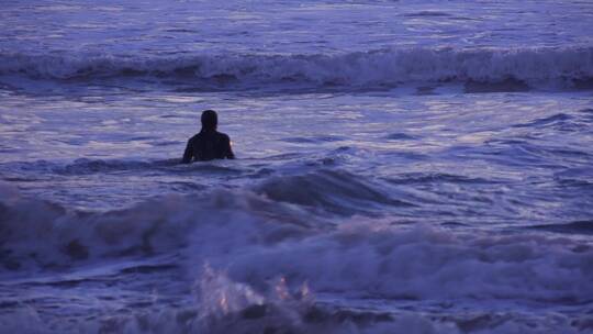 在日落时一名冲浪者穿过海浪