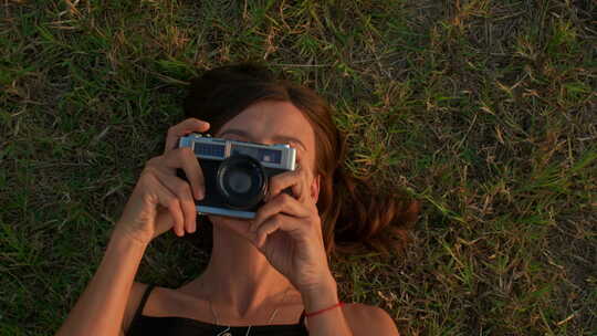 年轻女子躺在草地上用复古相机拍照