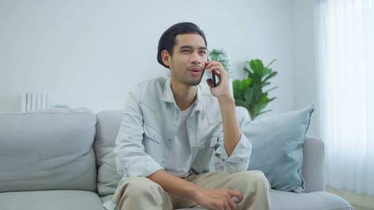 亚洲有魅力的男人坐在沙发上，在家里打手机。