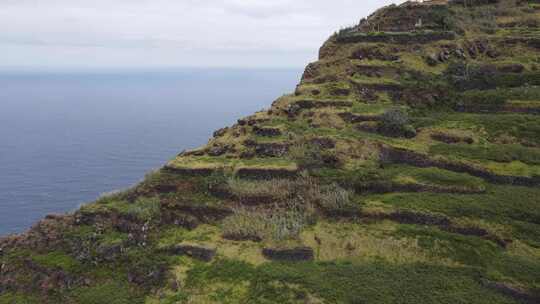 鸟瞰海边陡峭的梯田悬崖，三名徒步旅行者在