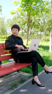 坐在公园长椅上使用笔记本电脑办公的美女