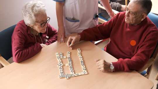护士在养老院食堂与老年男女玩多米诺骨牌