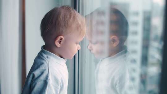童年在封锁期间一个在家隔离的小男孩看着窗外自我隔离