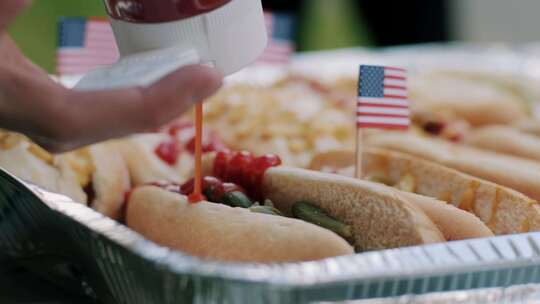 用美国国旗小牙签把番茄酱放在热狗上的人